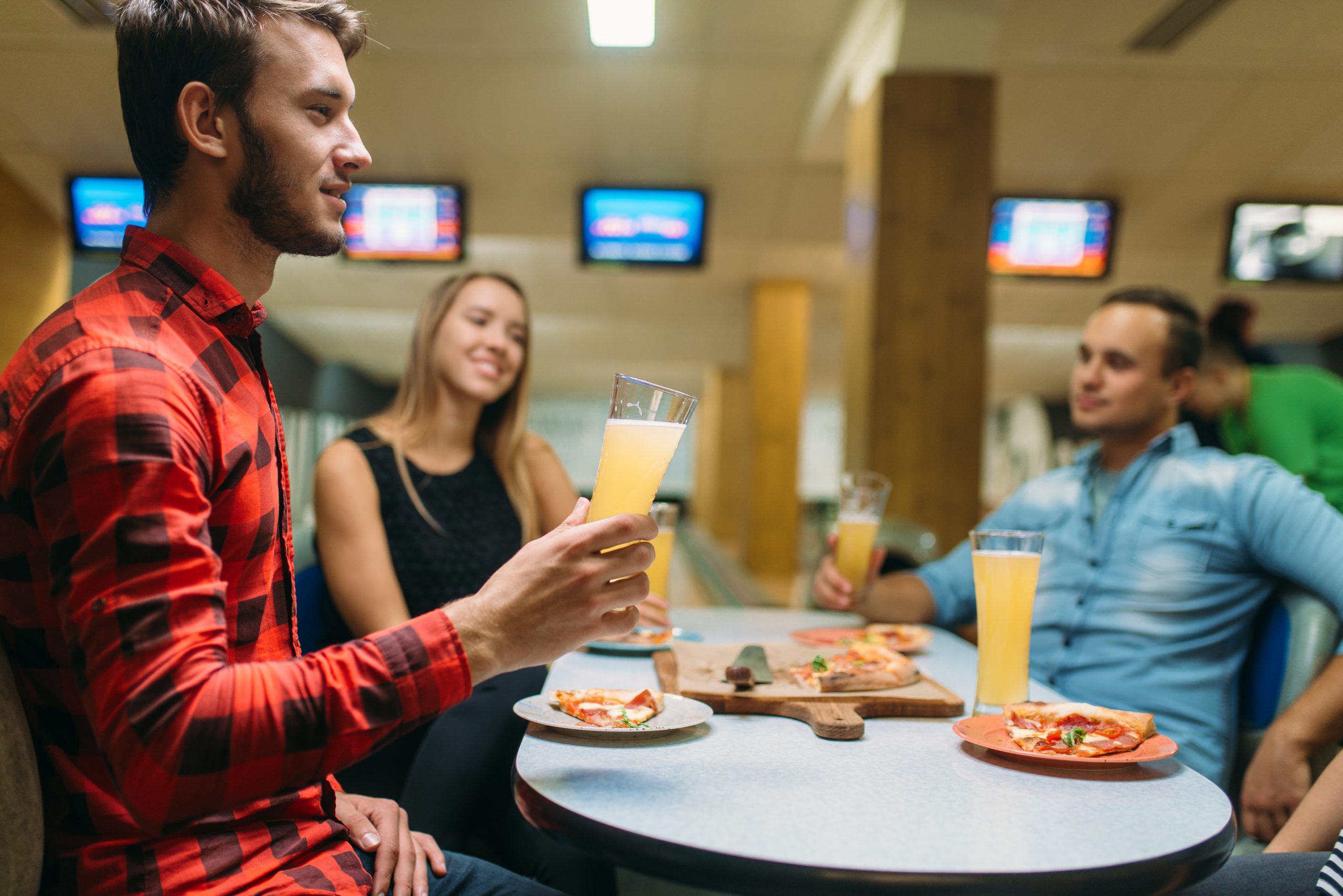 Friends drinks and eats pizza in bowling alley